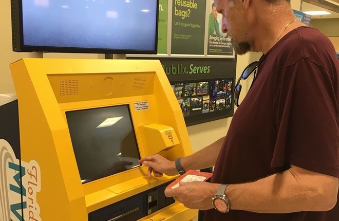 Person in maroon shirt operates yellow kiosk.